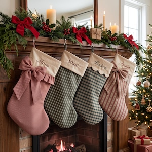 Puede incluir: Cuatro calcetines navideños personalizados colgados de una repisa de madera. Los calcetines presentan varios patrones que incluyen cuadros vichy rojos, rayas verdes, cuadros escoceses verdes y rayas rojas, cada uno con un puño color crema bordado con los nombres Mom, Dad, Hudson y Amelia.