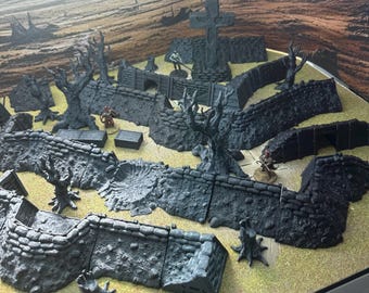 May include: A tabletop gaming terrain set featuring modular, gray, fortress walls, trees, and a cross. The set includes miniature figures and boxes, creating a detailed, immersive environment for role-playing games. The terrain is set on a yellow and brown surface.