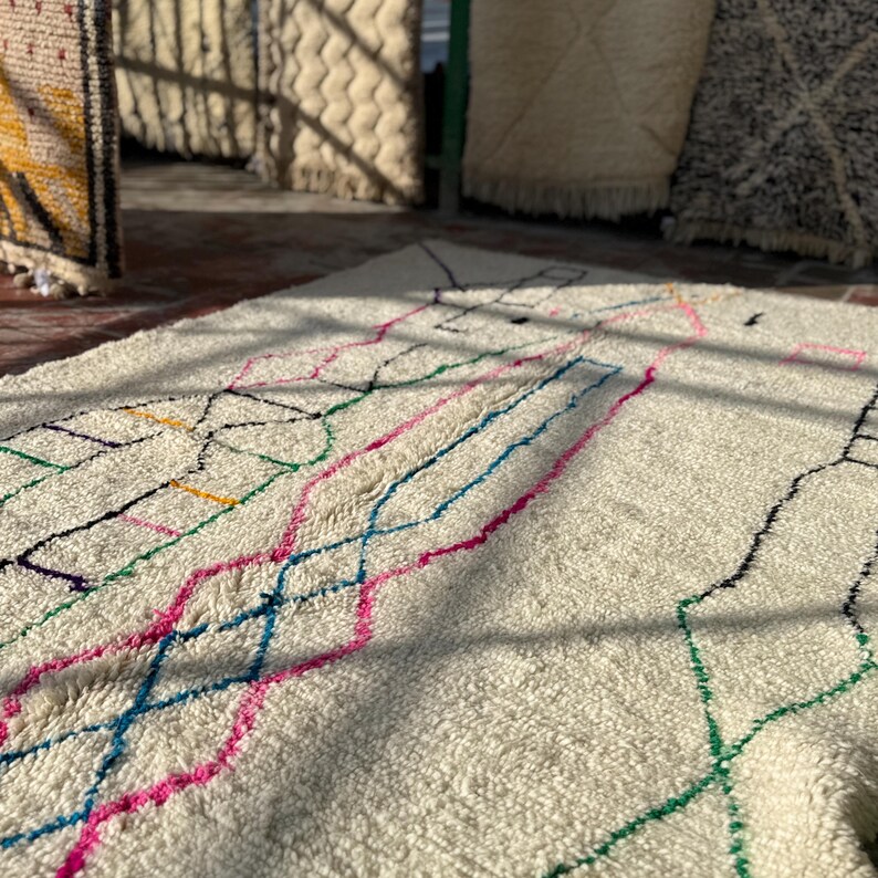 Puede incluir: Alfombra color crema con un dise&ntilde;o geom&eacute;trico en rosa, azul, verde, amarillo y negro. La alfombra tiene una superficie texturizada y se muestra con luz natural, mostrando su colorido patr&oacute;n.