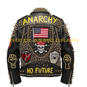 Puede incluir: Chaqueta de cuero negra con púas y tachuelas doradas. La parte trasera presenta la palabra "ANARCHY" en amarillo, una bandera estadounidense, una calavera y los huesos cruzados, y las palabras "NO FUTURE". Parches y cadenas añaden detalles.