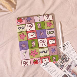 May include: A colorful tablet case with a patchwork design featuring strawberries, cowboy boots, bows, flowers, stars, and cocktail glasses. The case is in a grid pattern of pink, green, purple, and red squares. A white stylus is next to the case.