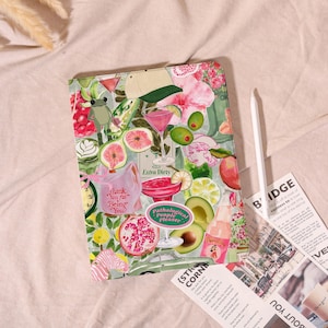 May include: A decorative tablet case with a collage of illustrations, including cocktails, fruit, and a frog. The case features the text "Extra Dirty", "Thank You for Being You", and "Pathological People Pleaser". A white stylus and printed papers are next to the case.