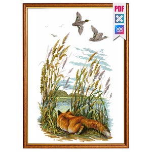 May include: Cross-stitch artwork of a fox resting near tall grass and a body of water. Two ducks fly overhead. The artwork is framed in a brown wooden frame. The image has a PDF icon in the upper right corner.