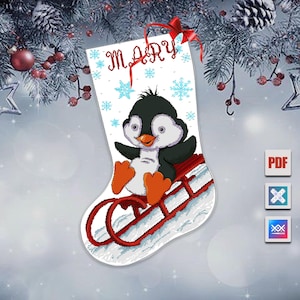 Puede incluir: Un calcetín navideño blanco con un diseño de punto de cruz que presenta un pingüino en un trineo rojo. El nombre "MARY" está bordado en rojo en la parte superior, con copos de nieve azules. Una cinta roja cuelga de la parte superior.