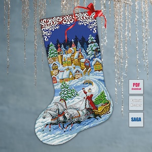 May include: A Christmas stocking with a detailed cross-stitch design. The scene depicts a snowy village with Santa Claus in a sleigh pulled by horses. The stocking has a blue background with a red ribbon at the top.