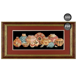 May include: A framed cross-stitch depicting a collection of Native American pottery. The pottery is in various shapes and sizes, with intricate patterns in shades of brown, orange, blue, and beige. The frame is a dark wood with a gold inner border.
