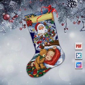 Op de afbeelding: Een kerstsok met een kruissteekontwerp. De sok toont een slapend kind met een teddybeer en een kerstman-scène met speelgoed. Bovenop is een rood lint bevestigd. De achtergrond heeft een sneeuweffect.