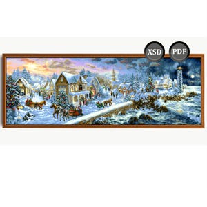 Op de afbeelding: Een ingelijste kruissteek die een winterse dorpsscène uitbeeldt met besneeuwde huizen, paardensleeën en een vuurtoren. Het kunstwerk heeft een warm kleurenpalet met een zonsondergang en kerstbomen.