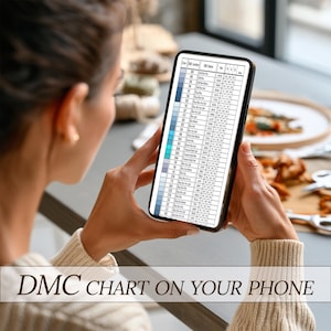 May include: A person holding a smartphone displaying a DMC color chart. The chart features rows of color swatches and corresponding DMC numbers. The phone screen is filled with text, and the image is set against a blurred background.
