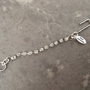 May include: A silver chain with clear rhinestones and a silver hook clasp. The chain has a small silver tag attached with the text "Alexi Blackwell" on it.