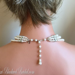 May include: A multi-strand pearl necklace with a silver clasp and a single strand of pearls extending from the back. The necklace is white and has a delicate, feminine look.
