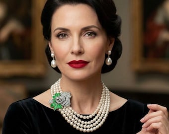 May include: A multi-strand pearl necklace featuring a large, silver-toned rose brooch with green enamel leaves. The necklace is paired with matching teardrop pearl earrings. The jewelry is worn with a black velvet top, creating a classic look.