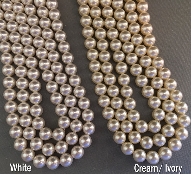May include: Two strands of pearl beads, one white and one cream/ivory. The beads are round and smooth.