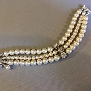May include: A triple strand pearl bracelet with silver clasps and rhinestone accents.