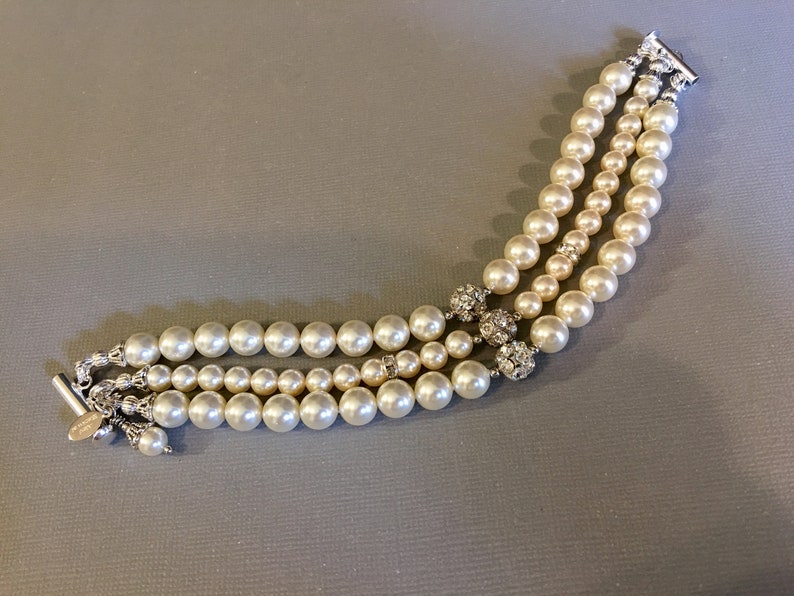 May include: A triple strand pearl bracelet with silver clasps and rhinestone accents.