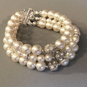 May include: A triple strand pearl bracelet with silver accents and rhinestone embellishments.