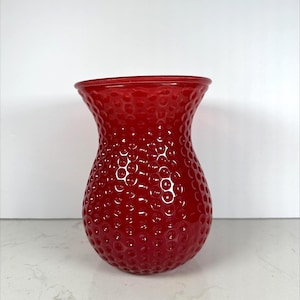 May include: A vibrant red glass vase with a textured, dimpled surface. The vase has a wide, flared opening and a rounded body. This decorative vase is suitable for displaying flowers or as a standalone accent piece.