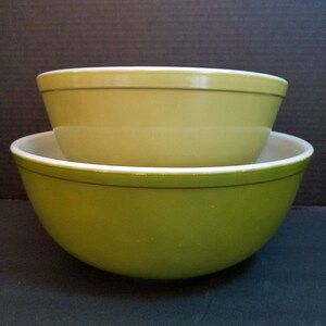 May include: Two green glass mixing bowls, one nested inside the other. The larger bowl is a darker shade of green, while the smaller bowl is a lighter shade of green.