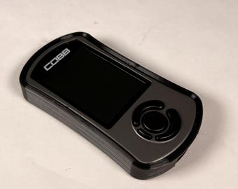 May include: A black and gray electronic device with a screen and buttons. The device has the word "COBB" printed on it. The device is rectangular with rounded edges and a circular button.