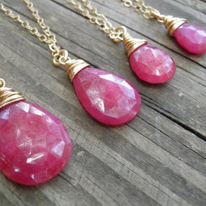 May include: Four gold chain necklaces with pink gemstone pendants. The pendants are wrapped in gold wire and have a faceted, teardrop shape.