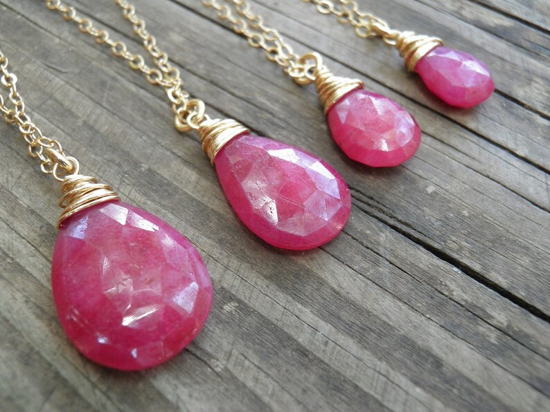 May include: Four gold chain necklaces with pink gemstone pendants. The pendants are wrapped in gold wire and have a faceted, teardrop shape.