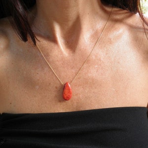 May include: A gold chain necklace with a teardrop-shaped red coral pendant.