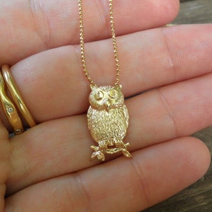 May include: A gold chain necklace with a detailed owl pendant. The owl is facing forward with its wings spread out.