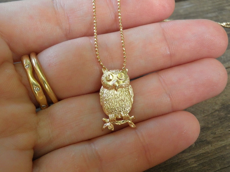 May include: A gold chain necklace with a detailed owl pendant. The owl is facing forward with its wings spread out.