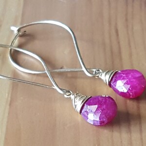 Pode incluir: Um par de brincos de prata com gotas de pedras preciosas facetadas cor de rosa envoltas em fio de ouro.