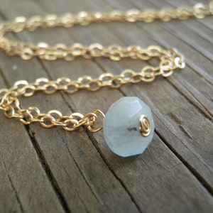 May include: A gold chain necklace with a light blue gemstone pendant. The pendant is faceted and has a gold wire wrapped around it.