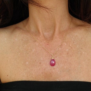 May include: A gold chain necklace with a teardrop-shaped pink gemstone pendant.