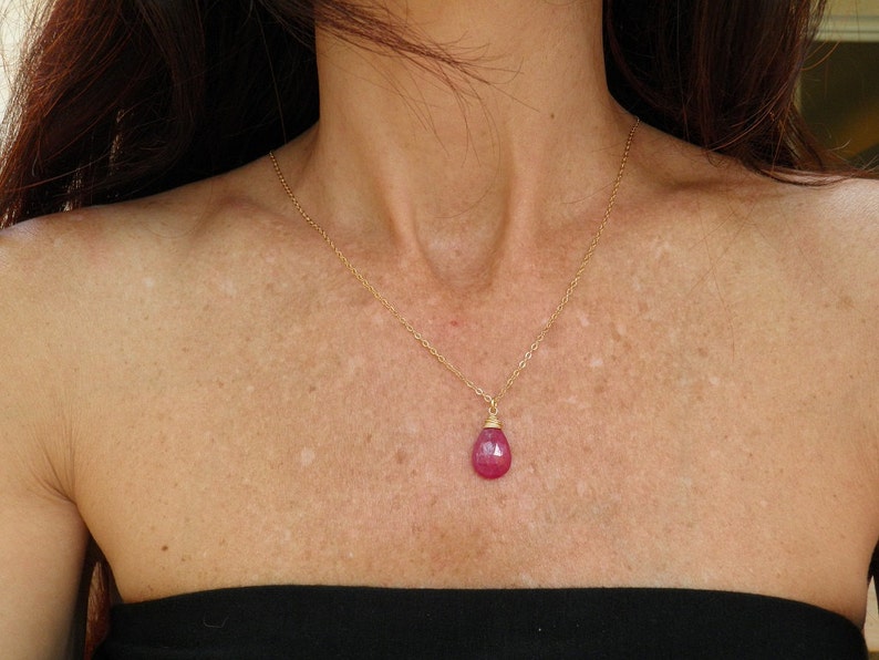 May include: A gold chain necklace with a teardrop-shaped pink gemstone pendant.