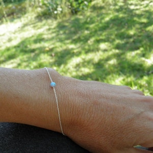 May include: A delicate silver chain bracelet with a single light blue gemstone bead.
