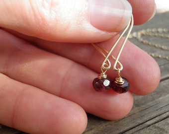 May include: A pair of gold dangle earrings with small, faceted, dark red gemstones.
