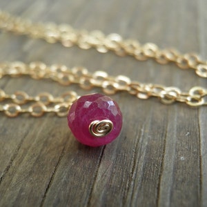 May include: A delicate gold chain necklace with a single, faceted, deep pink gemstone pendant.