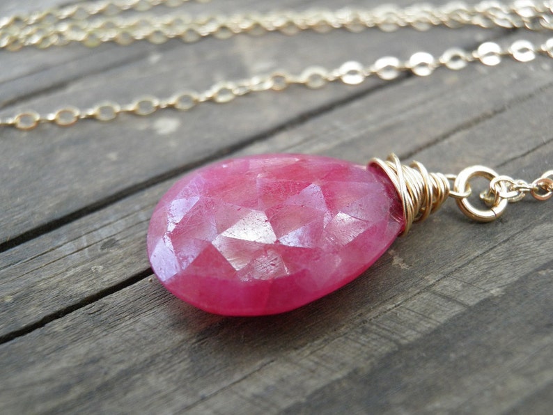 May include: A pink gemstone pendant necklace with a gold chain. The gemstone is faceted and has a teardrop shape.