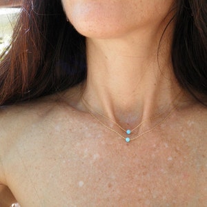 May include: A woman wearing a delicate gold chain necklace with two small turquoise stones.