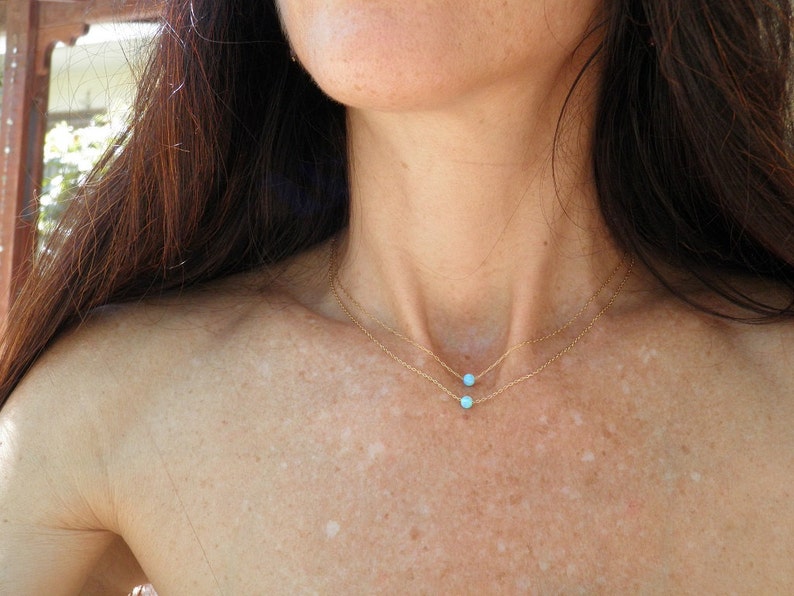 May include: A woman wearing a delicate gold chain necklace with two small turquoise stones.