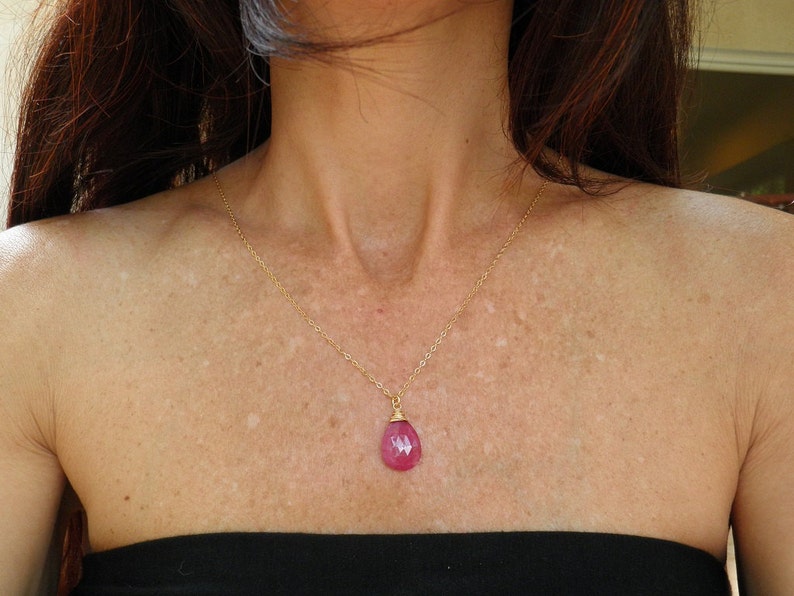 May include: A gold chain necklace with a pink gemstone pendant. The pendant is a teardrop shape and is set in a gold bezel.