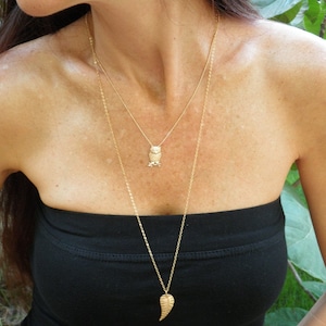 May include: A gold chain necklace with an owl pendant and a leaf pendant. The necklace is layered and worn by a person with long brown hair.