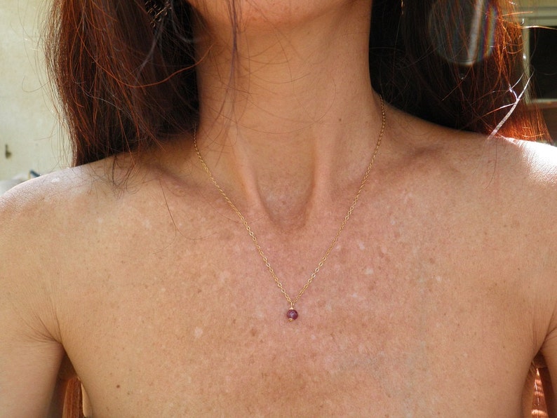 May include: A delicate gold chain necklace with a small, round, pink gemstone pendant.