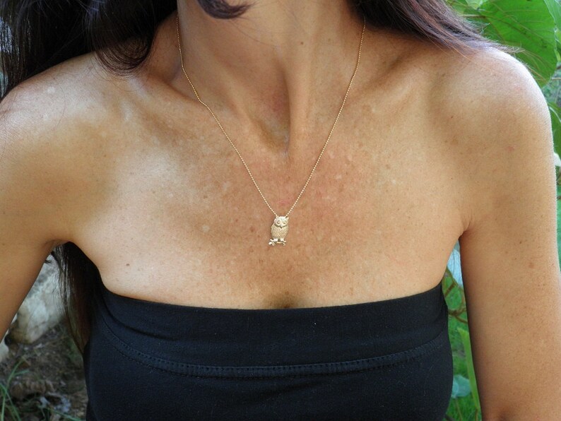 May include: A gold chain necklace with a small owl pendant. The owl is facing forward with its wings spread out.