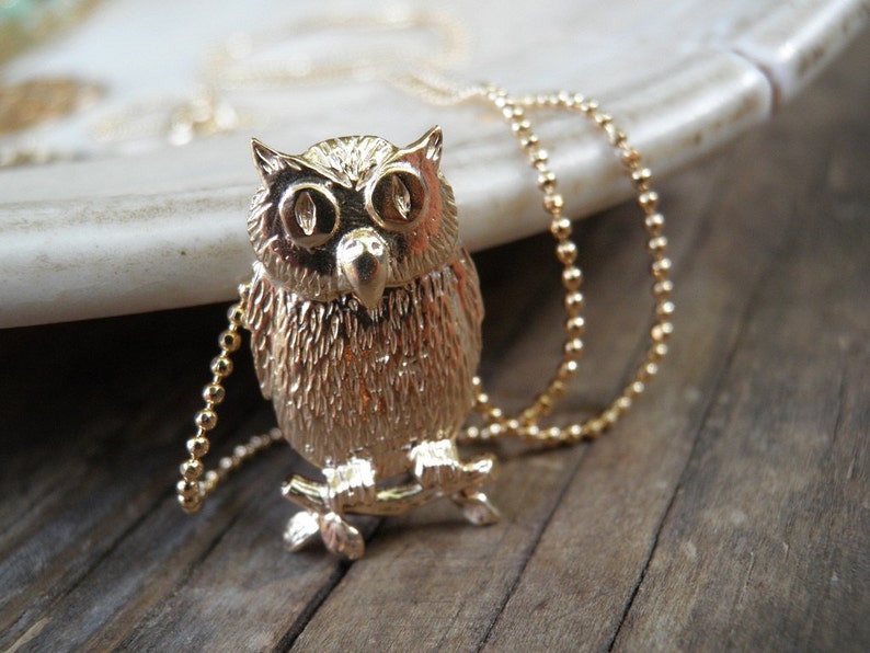 May include: A gold owl pendant necklace with a beaded chain. The owl is detailed with textured feathers and has large, round eyes.