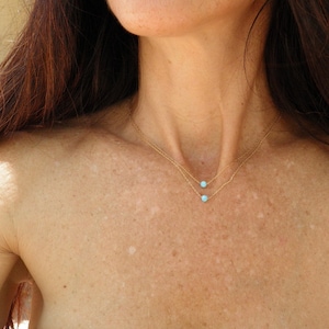 May include: A woman wearing a delicate gold chain necklace with two small turquoise stones.