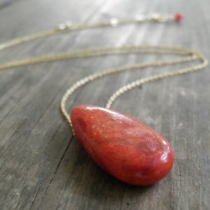 May include: A gold chain necklace with a teardrop-shaped red coral pendant.
