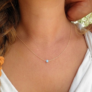 May include: A delicate gold chain necklace with a small, light blue opal pendant.