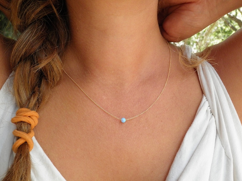 May include: A delicate gold chain necklace with a small, light blue opal pendant.