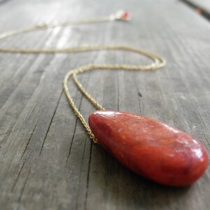 Puede incluir: Un collar de cadena dorada con un colgante de piedra roja en forma de lágrima.