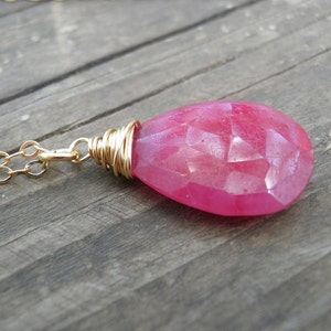 May include: A pink gemstone pendant necklace with a gold chain. The pendant is wrapped in gold wire and has a faceted, teardrop shape.