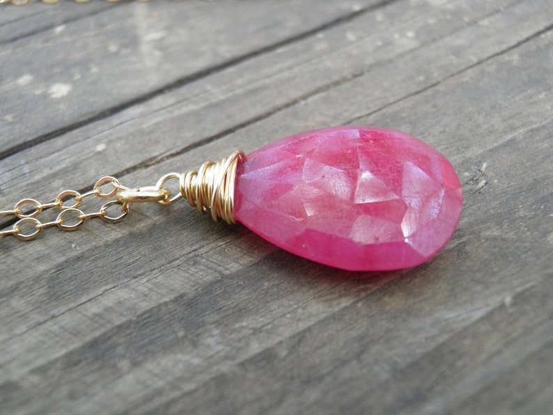 May include: A pink gemstone pendant necklace with a gold chain. The pendant is wrapped in gold wire and has a faceted, teardrop shape.